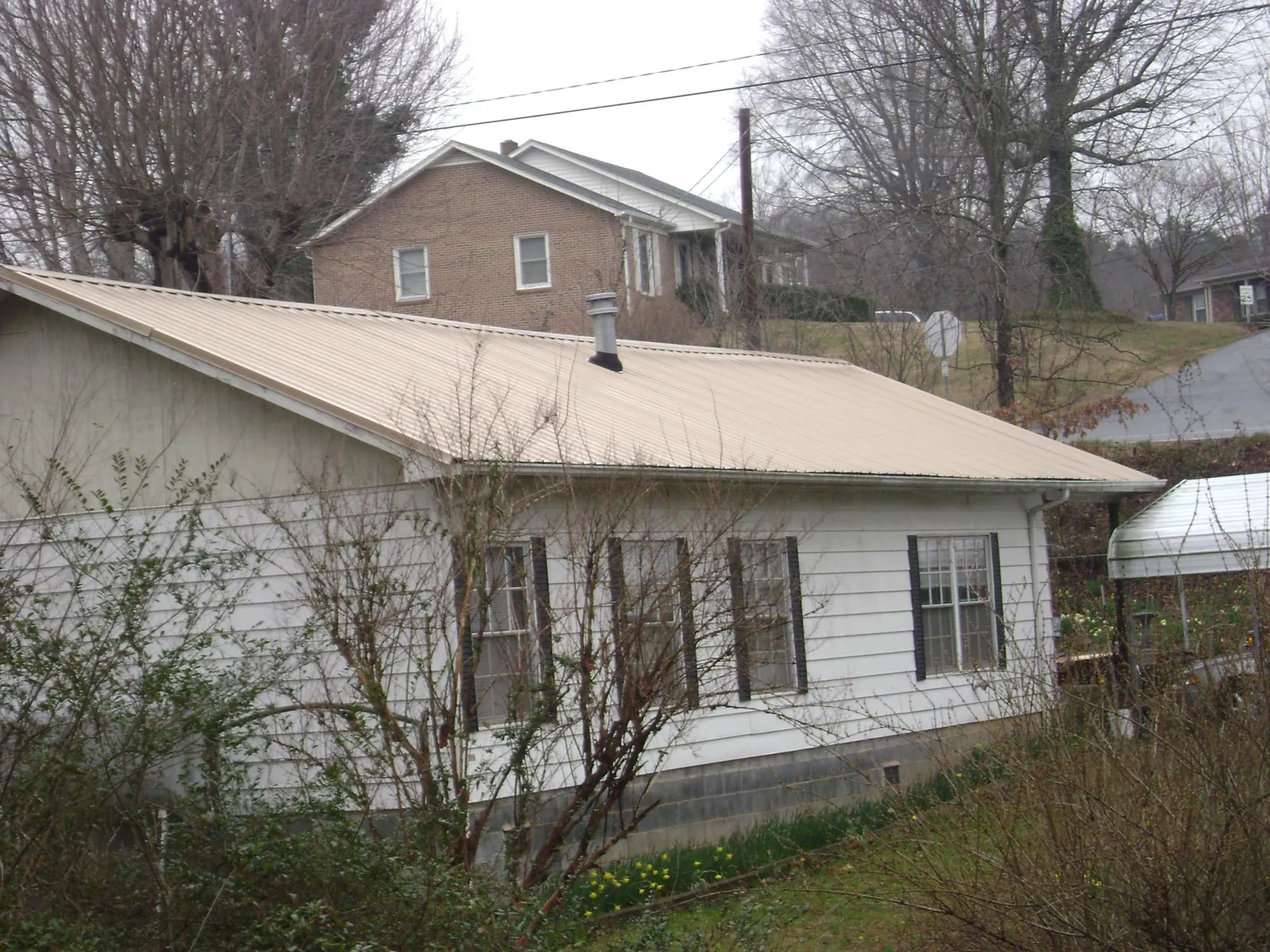 Tan metal roof on a white sided house set into a hillside — Commercial Roofing by Roofing Brothers in Yorktown